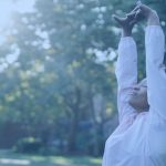 Person with their hands over their head, breathing deeply in the sunrise