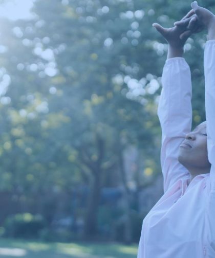 Person with their hands over their head, breathing deeply in the sunrise