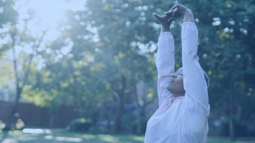 Person with their hands over their head, breathing deeply in the sunrise